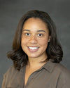 Portrait of Dr. Jessica Hippolyte wearing a brown top against a gray background