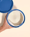 A hand holding an opened can of Nara's Organic Whole Milk Infant Formula, top down.