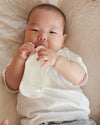 A baby lying down on a blanket, bottle feeding.